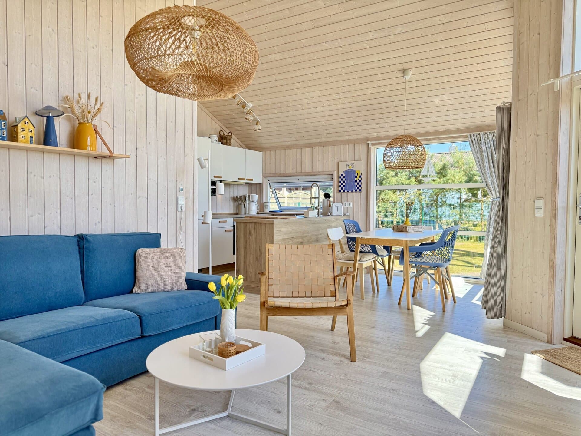 Gemütliches Wohnzimmer mit offener Küche und großen Fenstern, viel Tageslicht.